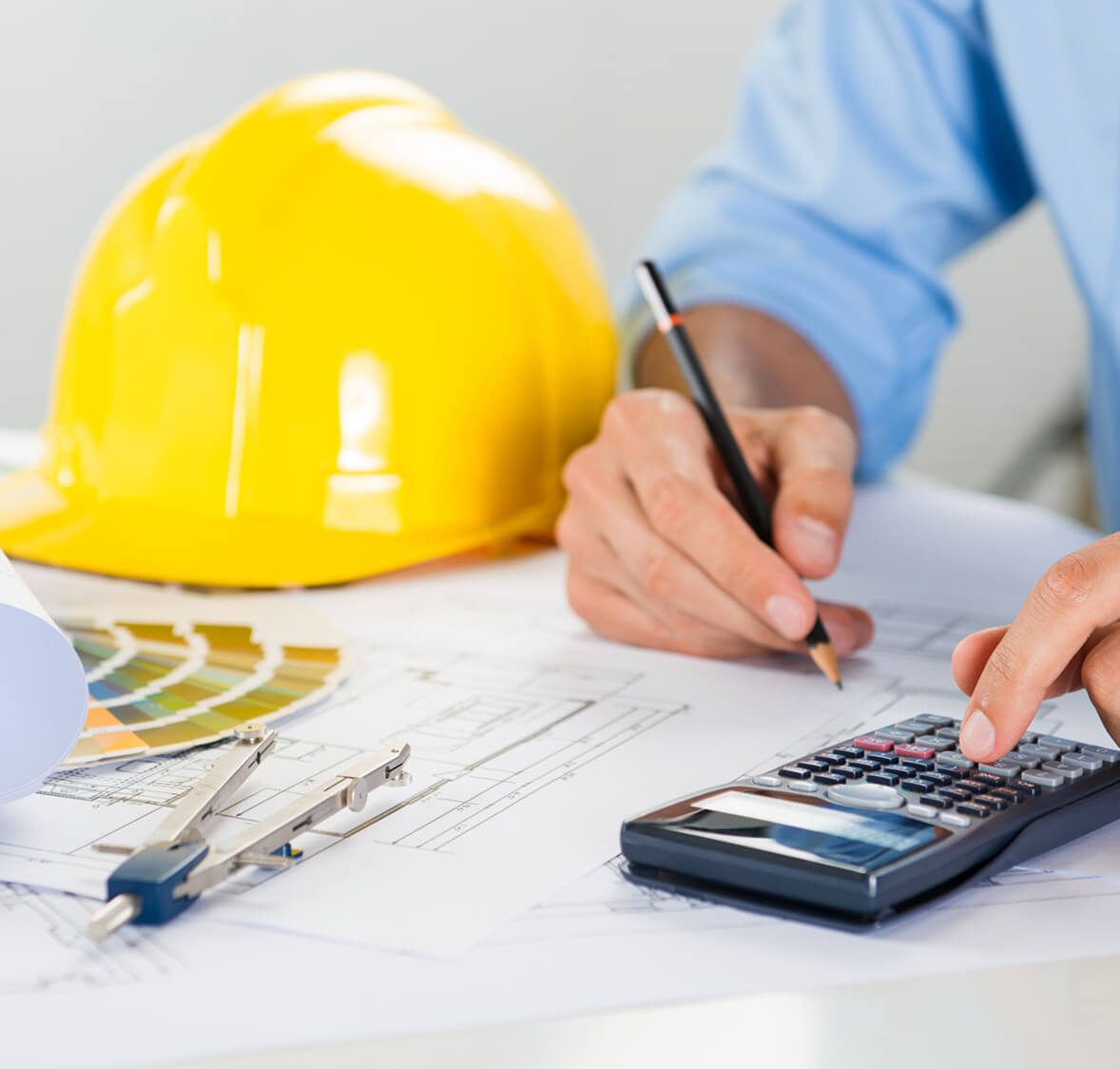 Engineer calculating on blueprint with helmet nearby.