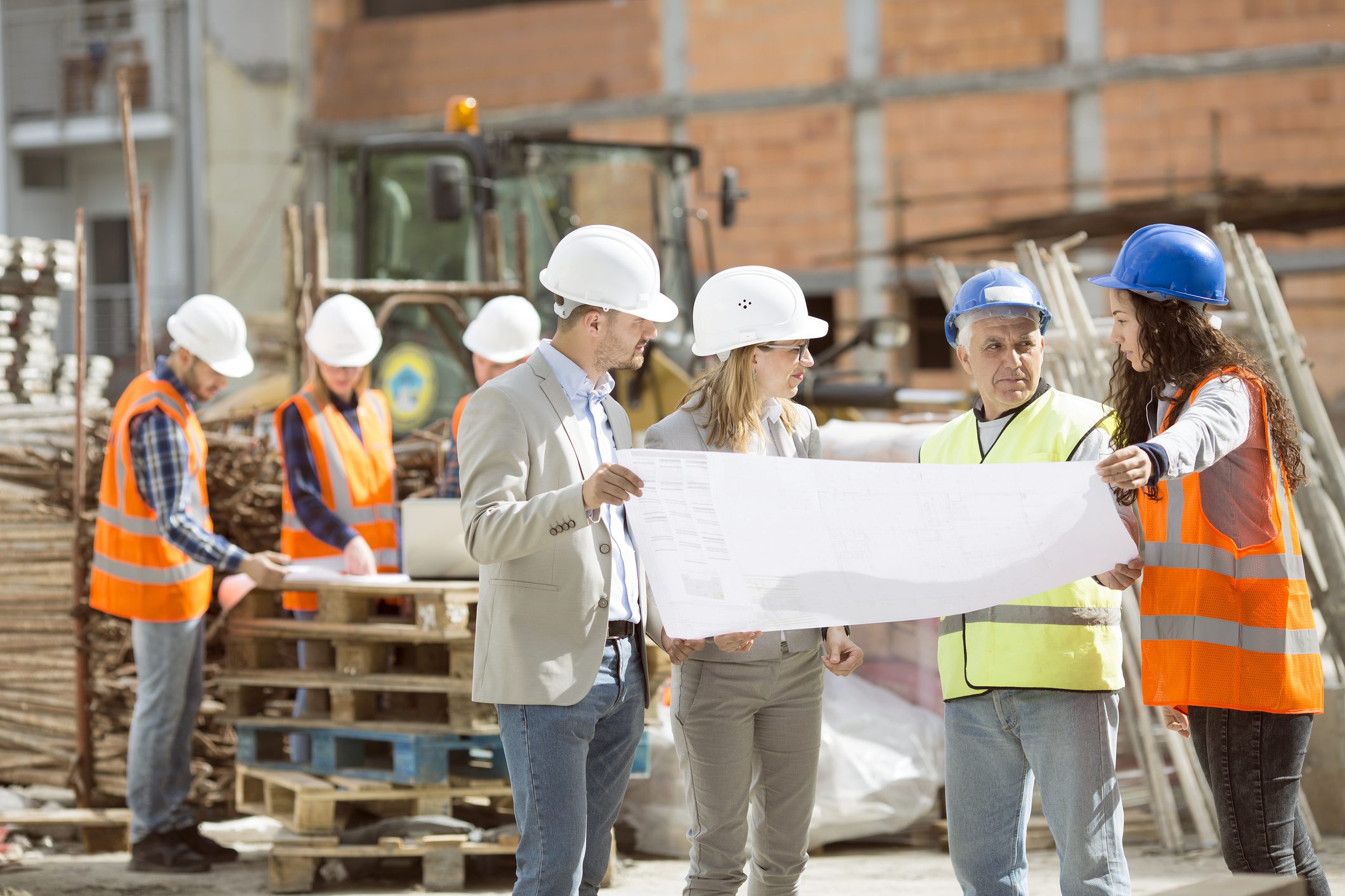 Group Construction workers looking at blueprints on construction site A group of people in hard hats and safety vests.